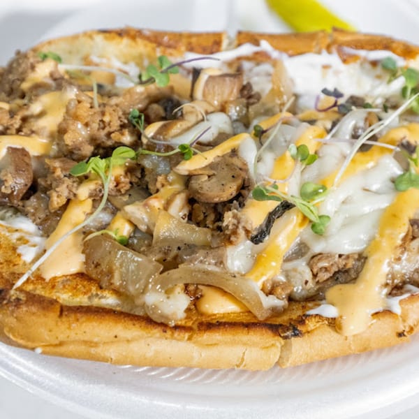 Vegan cheesesteak from Plant Bae, topped with melted cheese, onions, mushrooms, and microgreens.