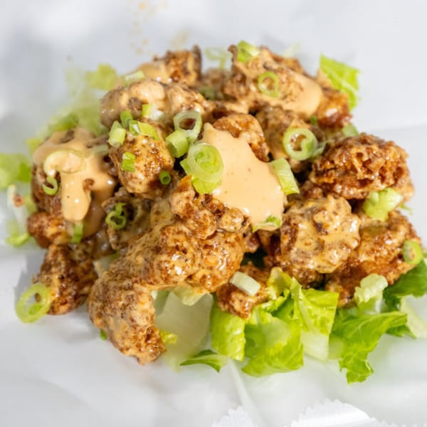 Plant Bae's vegan bang bang shrimp, drizzled with sauce and garnished with green onions over lettuce.