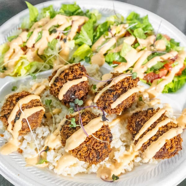 Plant Bae's vegan dish with crispy falafel, rice, and a fresh green salad, drizzled with sauce.