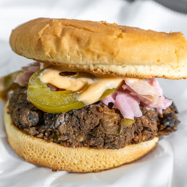 Close-up of a Plant Bae vegan burger with a thick patty, pickles, pink onions, and sauce.